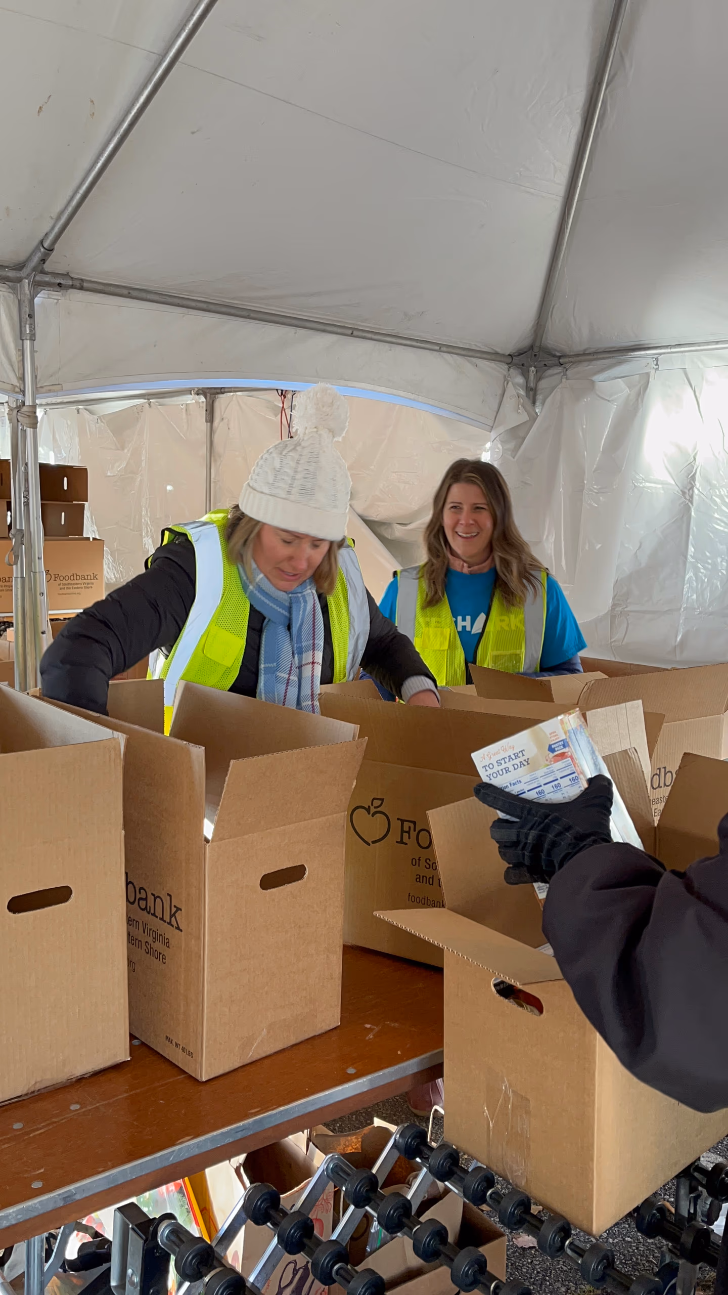Women volunteering at Foodbank of Southeastern Virginia, packing boxes for community food distribution, with TechArk branding visible on a shirt.